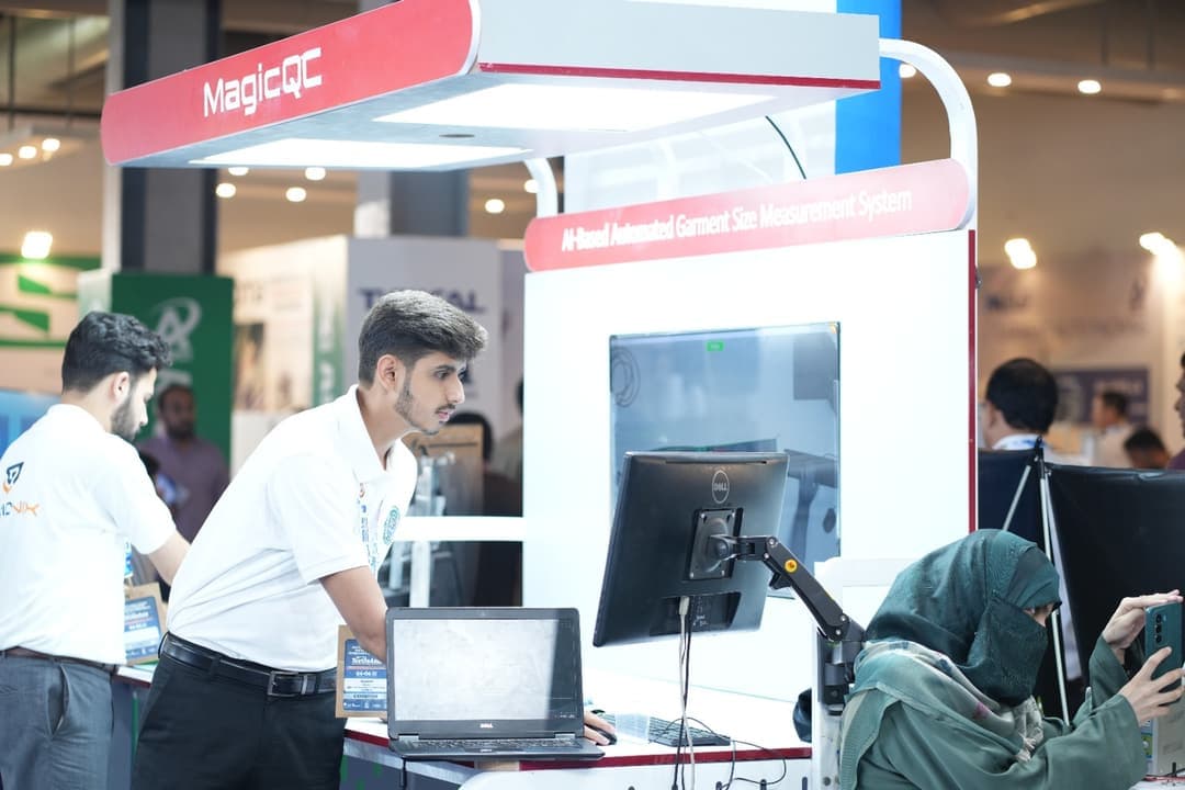 Hamza demonstrating the MagicQC size-measurement rig to a visitor at the TextileAsia stand.